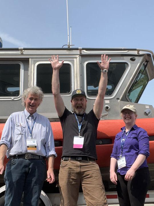 three people st和ing in front of a boat